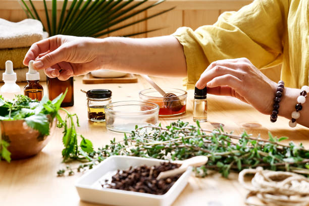 Une femme prépare une séance d'aromathérapie à table avec des herbes médicales diffuseur d'huiles essentielles, différents types d'huiles et d'essences. Concept d'aromathérapie et de médecine alternative. Remèdes naturels.
